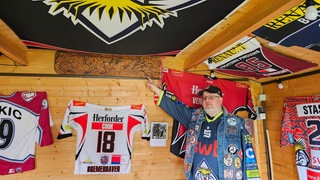 Ein Mann zeigt in einem Schuppen Trikots der Fischtown Pinguins.