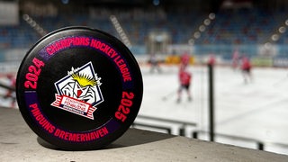 Auf einem Puck in der Eisarena steht "Champions Hockey League Pinguins Bremerhaven" geschrieben. 