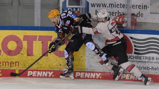 Ein Eishockeyspieler tackelt einen anderen -spieler gegen die Bande.