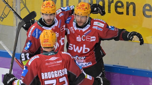 Eishockey-Spieler der Fischtown Pinguins um Jan Urbas in roten Trikots umarmen sich jubelnd nach einem Tor.