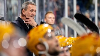 Pinguins-Coach Thomas Popiesch steht während des Spiels an der Bande und hält sich nachdenklich die Hand ans Kinn.