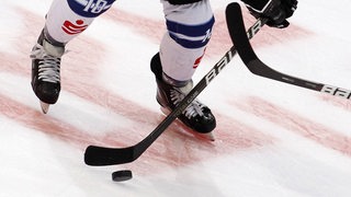 Nahaufnahme eines Eishockey-Pucks, um den auf dem Eis zwei Spieler mit ihren Schlägern kämpfen.