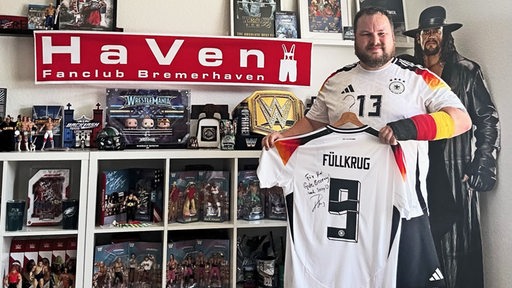 Ein Fußballfan mit gebrochenem Handgelenk hält ein Nationalelf-Füllkrug-Trikot mit Unterschrift in die Kamera.