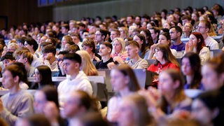 Erstsemester sitzen in einem vollgefüllten Höhrsaal an ihrem ersten Studientag.