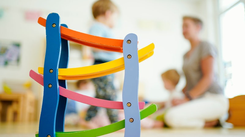 Eine Erzieherin spielt in einer Kindertagesstätte hinter einer Rollbahn mit Kindern.