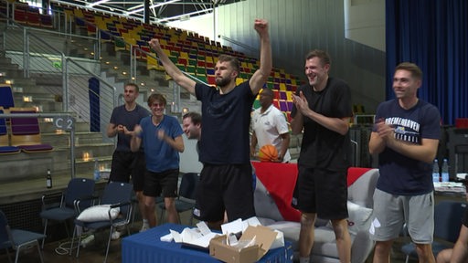 Zu sehen ist dei Mannschaft der Bremerhavener Eisbären, wie sie das Deutsche Basketballspiel verfolgt.