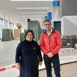 Zwei Personen stehen in einer Halle mit verhüllten Gegenständen.