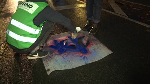 Zwei Personen sprühen ein Fahrradsymbol auf die Straße.