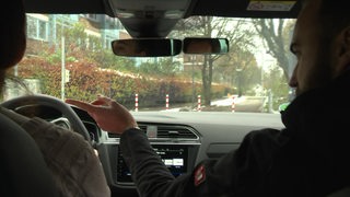 Der Fahrlehrer sitzt mit seiner Fahrschülerin im Fahrschul Auto. 