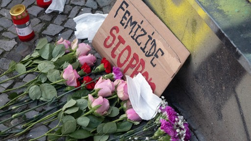 Blumen und Grablichter liegen vor einem Schild "Femizide stoppen"