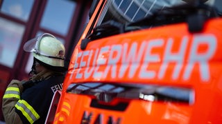 Eine Einsatzkraft der Feuerwehr steht neben einem Einsatzfahrzeug der Feuerwehr 