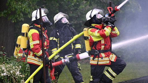 Feuerwehrmänner im Einsatz halten Schläuche in den Händen.