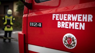 "Feuerwehr Bremen" steht auf der Tür eines Einsatzfahrzeuges. Im Hintergrund steht ein Feuerwehrmann.