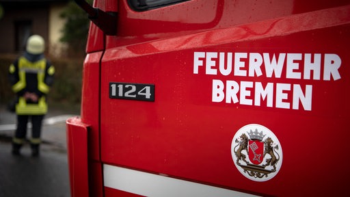 "Feuerwehr Bremen" steht auf der Tür eines Einsatzfahrzeuges. Im Hintergrund steht ein Feuerwehrmann.