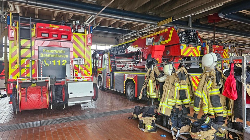 In einer Hall stehen Feuerwehrautos  und Garderoben mit Uniformen.