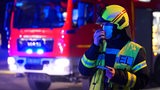 Ein Feuerwehrmann steht während eines Einsatzes vor einem Feuerwehrwagen.