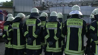 Eine Gruppe Feuerwehrmänner, die mit dem Rücken zur Kamera stehen.