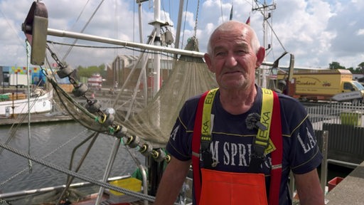 Der Krabbenfischer Hans-Joachim Reim steht vor seinem Fischerboot am Hafen.