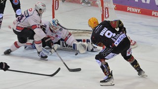 Ein Eishockey-Spieler schießt den Puck aufs Tor. Der Torwart schmeißt sich davor.