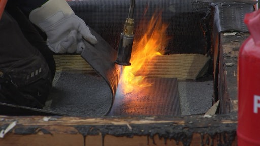 Eine Dachmatte wird von einem Handwerker flambiert und geschmolzen zum Festkleben. 