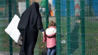 Eine Frau geht mit ihren Kinder durch einen Zauneingang (Archivbild)