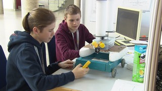 Zwei Jugendliche sitzen an einem Schreibtisch. Vor ihnen steht ein Flettner-Rotor: ein umweltfreundlicher Schiffsantrieb.