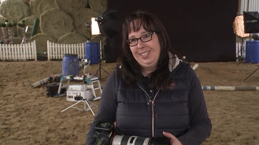 Andrea Zachrau, Pferdefotografin, steht in einer Reithalle mit ihrere Kamera in den Händen.