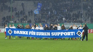 Die Spielerinnen des HSV stehem im Volksparkstion auf dem Platz und halten ein Banner hoch, auf dem "Danke für euren Support" steht.