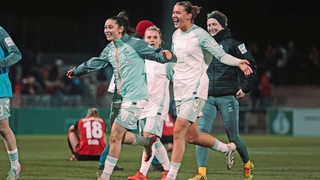 Werders Fußballerinnen Larissa Mühlhaus und Amani Mahmoud rennen lachend mit ausgebreiteten Armen nach dem Einzug ins Pokal-Halbfinale aufs Spielfeld. 