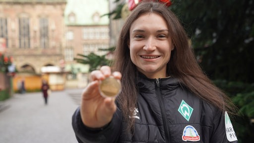 Werder-Stürmerin Sophie Weidauer hält strahlend auf dem Bremer Weihnachtsmarkt ihre Medaille für das "Tor des Monats" der ARD-Sportschau in die Kamera.