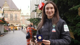 Werder-Stürmerin Sophie Weidauer hält strahlend auf dem Bremer Weihnachtsmarkt ihre Medaille für das "Tor des Monats" der ARD-Sportschau in die Kamera