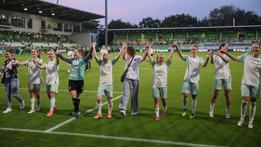 Werders Fußballerinnen bilden vor der Fankurve im Wolfsburger Stadion und feiern gemeinsam ihren ersten Punkt beim VfL.