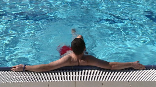 Eine Person die sich am Beckenrand im Freibad festhält von hinten. 