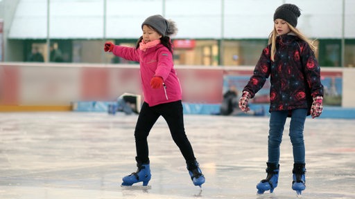 Zwei Mädchen fahren mit Schlittschuhen auf einer Eisbahn 