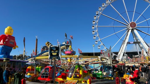 Das Riesenrad und verschiedene Fahrgeschäfte mit Besuchern auf dem Bremer Freimarkt bei strahlendem Wetter.