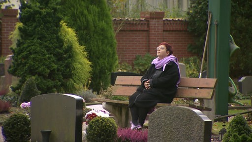 Die Bremer Pastorin Hannah Detken sitzt auf dem Friedhof auf einer Bank zwischen den Gräbern.