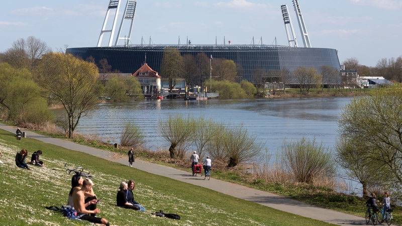 Menschen geniessen die Sonne am Osterdeich an der Weser, hinten das Weserstadion vom SV Werder Bremen.