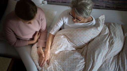 Eine junge Frau sitzt am Bett einer älteren Frau und hält ihre Hand (Symbolbild)