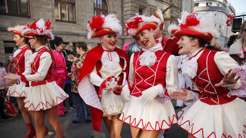 Junge Frauen, die als Funkenmariechen verkleidet sind, laufen bei einem Karnevalsumzug mit.