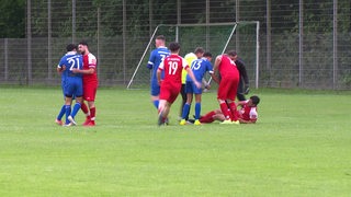 Auf einem Fußballspielfeld sind zwei Mannschaften zu sehen. Ein Junge liegt auf dem Boden und seine Mitspieler stehen um ihn herum.