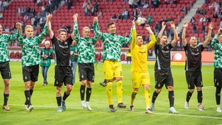 Die Werder-Spieler halten sich aufgereiht vor der Fankurve im Mainzer Stadion an den Händen und feiern nach dem Sieg.