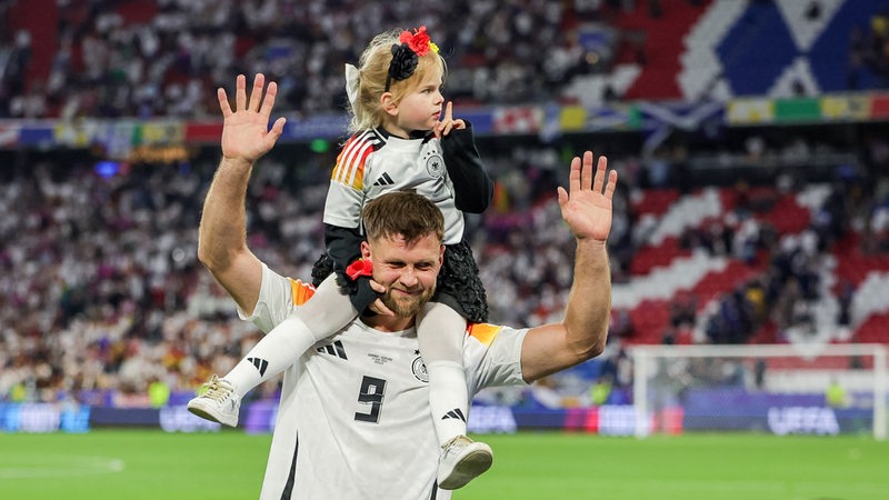 Der deutsche Nationalspieler Niclas Füllkrug trägt jubelnd nach dem Auftaktsieg gegen Schottland seine kleine Tochter auf den Schultern durchs Stadion.