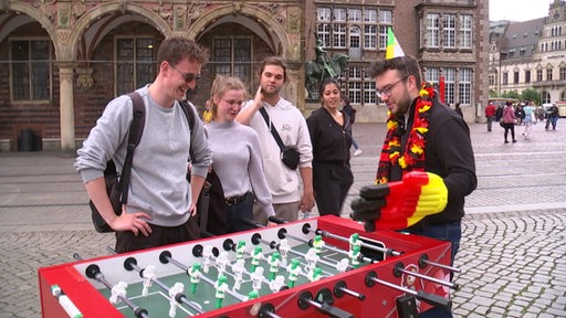 Auf dem Bremer Markplatz stehen mehrere Menschen um einen Tischkicker herum. 