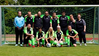 Menschen in Fußballkleidung stehen und hocken in zwei Reihen in einem Tor.