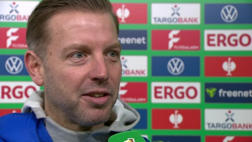 Darmstadt-Trainer Florian Kohfeldt steht nach dem Pokalspiel gegen Werder lächelnd vor einer Werbewand beim Interview.