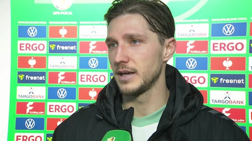 Werder-Profi Niklas Stark steht nach dem Pokal-Aus in Bielefeld vor einer Werbewand beim Interview.
