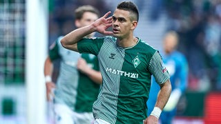 Werder-Stürmer Rafael Borré hält sich bei seinem Torjubel in Richtung der Fans auffordernd die Hand ans Ohr.