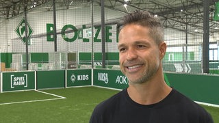 Werders ehemaliger Spieler Diego steht lächelnd in Werders Fußballhalle bei einem Interview.