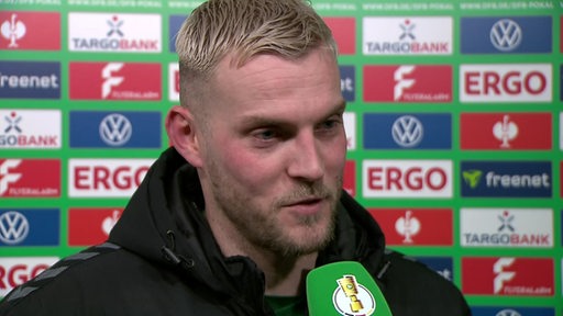 Werder-Stürmer Marvin Ducksch steht nach dem Pokalspiel gegen Darmstadt vor einer Werbewand beim Interview.