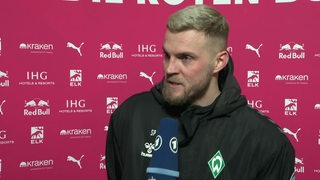 Werder-Stürmer Marvin Ducksch steht nach der Niederlage gegen Leipzig vor einer pinkfarbenen Werbewand beim Interview.